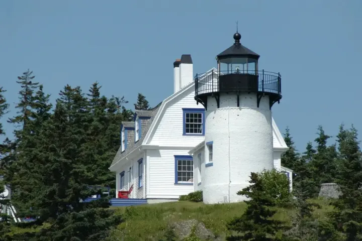 White lighthouse with attached house surrounded by trees on a sunny day.